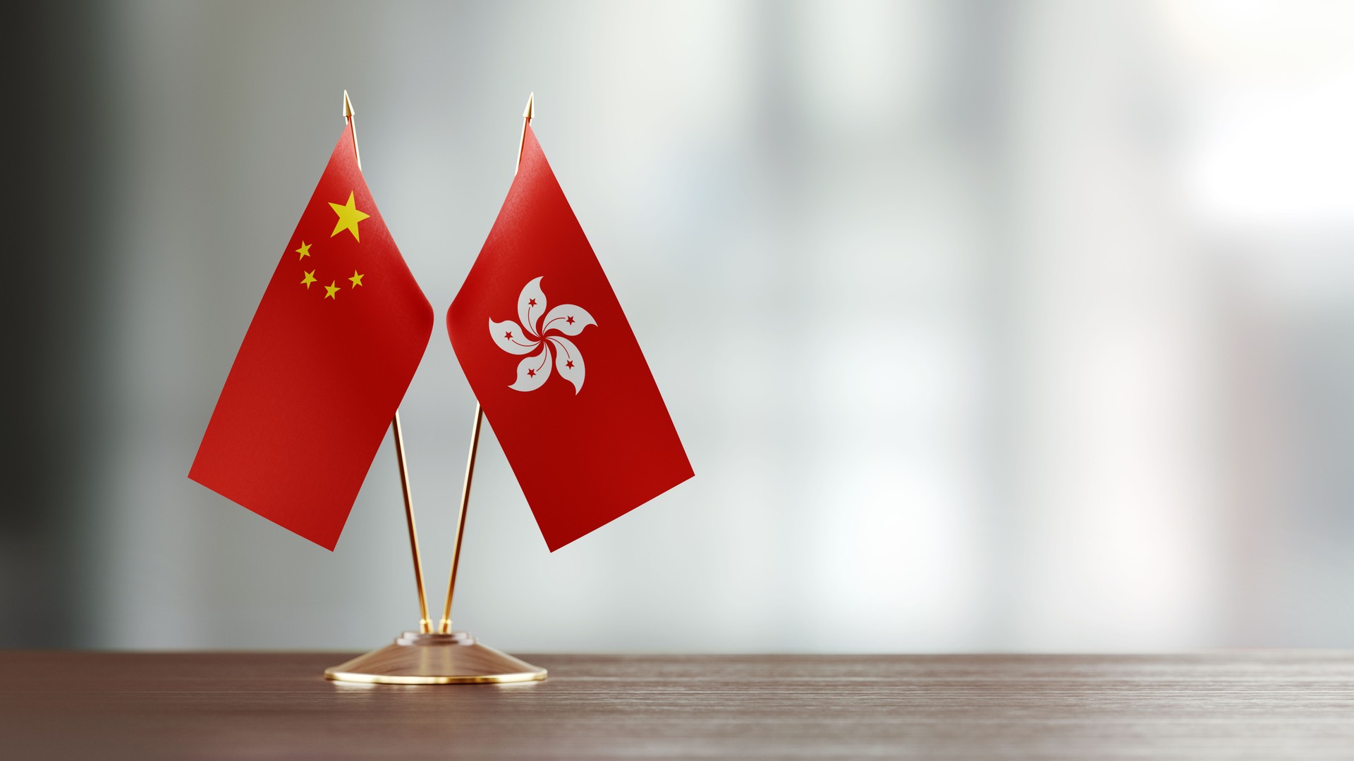 Chinese And Hong Kong Flag Pair On A Desk Over Defocused Background